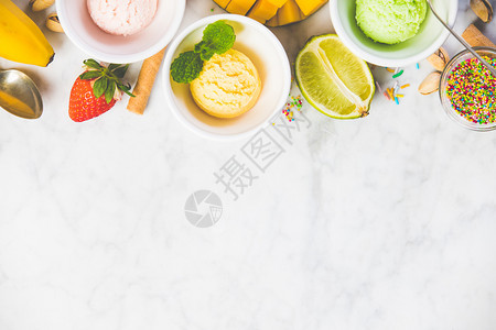 白碗中的冰淇淋和白大理石底的新鲜成分顶部视图粉色草莓黄芒果或香蕉和绿色石灰茶或活塞图片