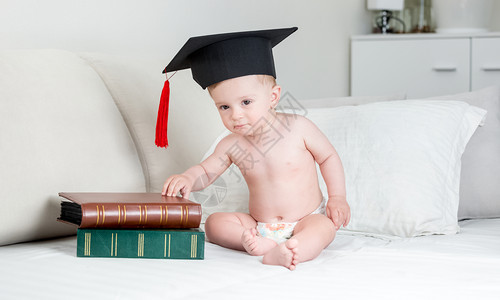 用尿布和毕业帽坐在床上带书的铺用的床上图片