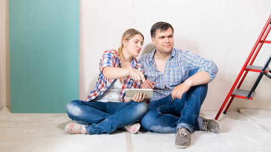 幸福的情侣坐在他们新房子的地板上从网商店中选择家具图片