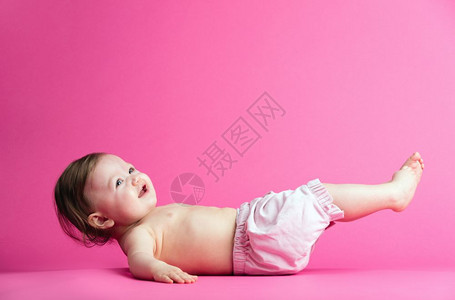婴儿女孩躺在她背上试图站起来粉色背景童年图片