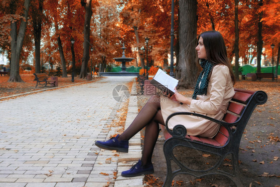 坐在公园长椅上的女孩在大腿拿着一本书在公园里的一个学生在看本书图片