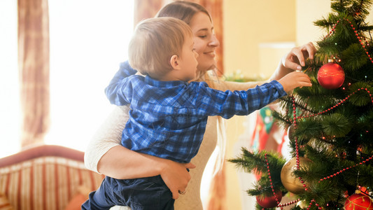 微笑的年轻女子肖像与她幼儿子一起在圣诞树上挂着芭饼微笑的年轻女子肖像与她幼儿子在圣诞树上挂着芭饼图片