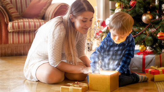 令人兴奋的幼儿男孩把圣诞礼物从发光的魔法礼品盒中拿出来图片