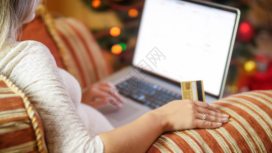妇女坐在圣诞树旁边笔记本电脑上浏览网商店图片