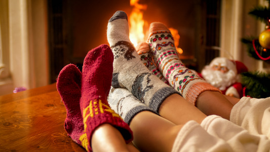 3人穿着编织的羊毛袜子在小屋壁炉上变暖3人穿着编织的羊毛袜子图片