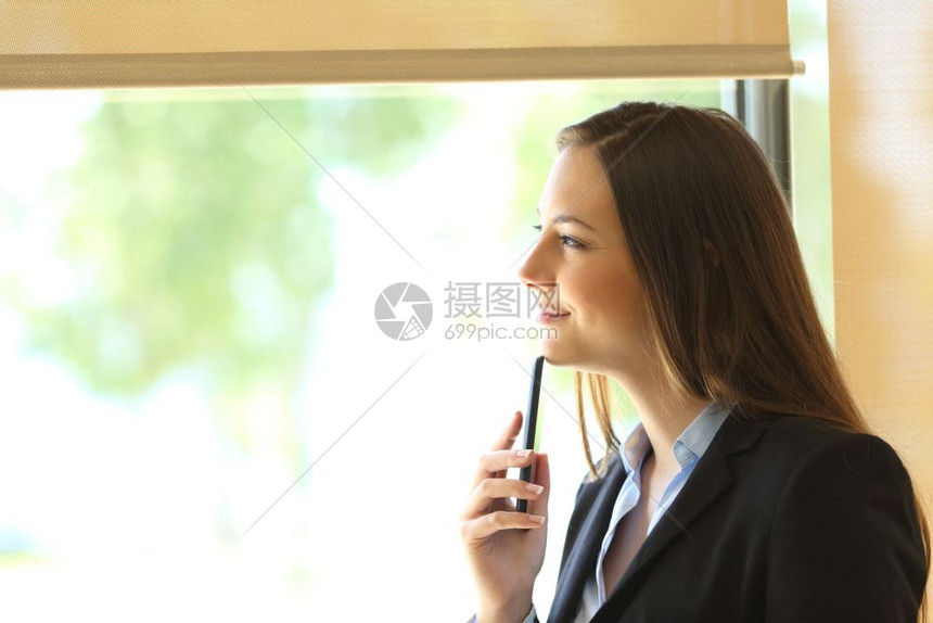 一位身穿西装思考的女商人侧面观透过办公室的窗户看外
