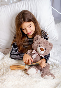 梦想的家小女孩躺在床上和她最喜欢的泰迪熊躺在床上睡觉前读一本书背景