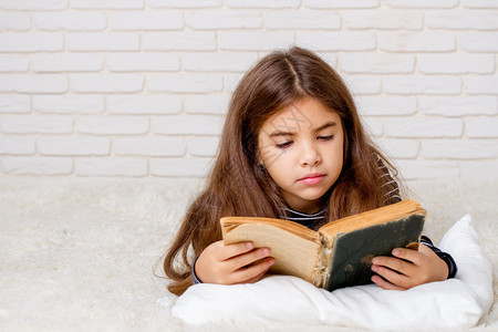 一个小女孩躺在床上拿着一本大旧书在她面前看图片