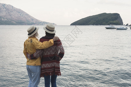 两个穿着帽子的黑发金女孩站着看夏天的海旧式斯塔格兰风照片图片