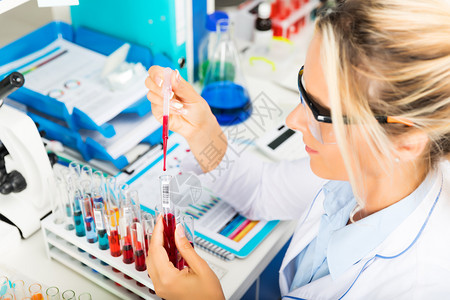 年轻有吸引力的女科学家身着保护眼镜的年轻有吸引力女科学家在化实验室中将红色液体物质用管子和放入试验图片