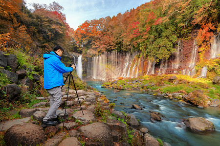 亚洲摄影师拍瀑布的地貌照片秋天在Yamaashi的藤川口子附近落叶日本有蓝天背景的树木图片