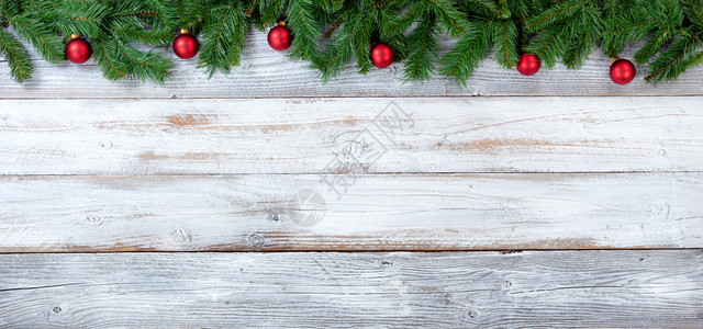 圣诞长绿树枝和白旧木上红装饰品的顶端边界图片