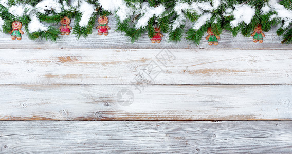 雪覆盖了圣诞长绿树枝的顶端以及白旧木头的饼干装饰品图片