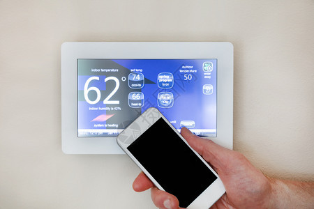 男手持智能电话操作家庭自动调温器的供暖或冷却图片