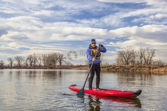 高官在科罗拉多州秋天或冬季的湖边划着一个可充气的站台爬上桨板图片