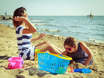 父母亲和孩子在沙滩上挖洞暑假放松家庭母亲和女儿在沙滩上玩得开心图片