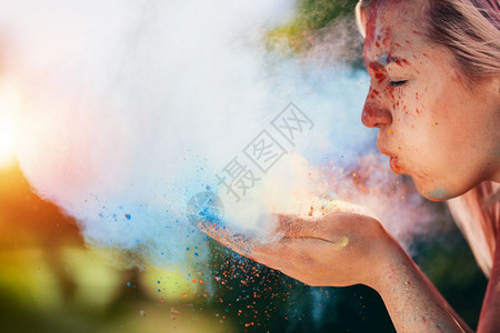 女人吹着多彩的辣椒粉制造了多彩的灰尘云欢乐节和庆祝活动图片