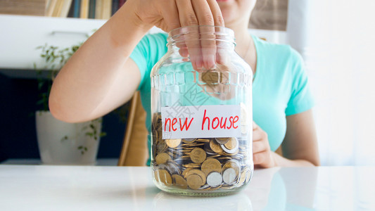 年轻女将硬币扔入玻璃罐中并节省购买新房子的钱图片
