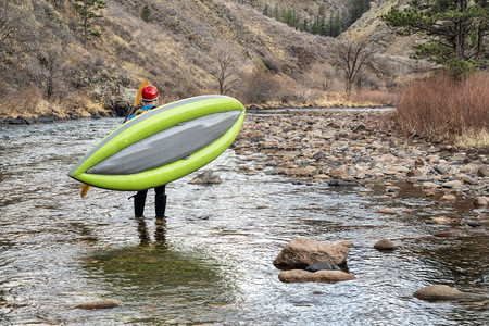 初春在科罗拉多州福特恩斯河岸的Poudre河上在山岸携带可充气白水皮艇的板车图片