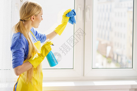 穿着黄色手套的年轻女士在家里用抹布和喷雾洗涤剂擦窗户图片
