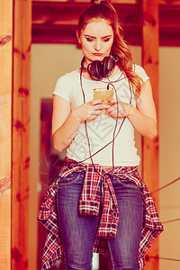 年轻女孩使用电话监听音乐耳机选择轨有耳机的女人在智能手机上选择音乐图片