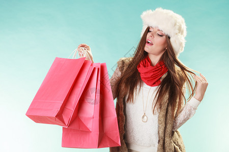 穿着毛帽的年轻女孩穿着工作室蓝色冬季时装服销售买包的女人冬季时装背景图片