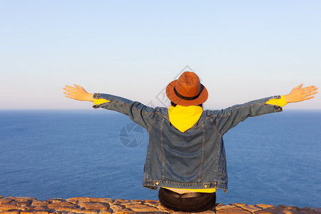 穿着旅行服和帽子坐着看蓝色的海洋和天空旅行概念照片穿旅行服和帽子坐着看蓝色的海洋和天空图片