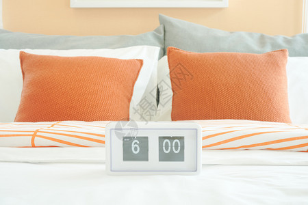 床上的白闹钟和背着橙色枕头的图片