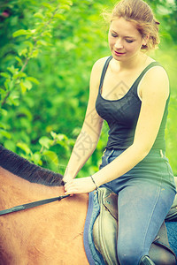 年轻女坐在马上骑阳光明媚的春天花园里骑马年轻女坐在马上图片