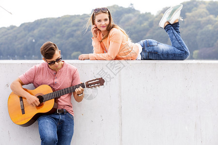 吉他家和的缪斯年轻男人和躺在墙上有着风景背的女孩弹吉他图片