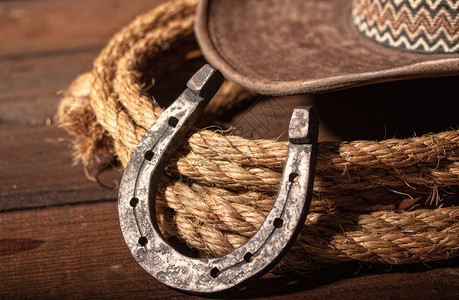 古老的马蹄铁就在经典牛仔帽和黑色木头背景的拉索旁边图片