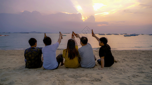 泰国人亚洲朋友串连啤酒瓶子在日落时夏海滩或边庆祝节日图片