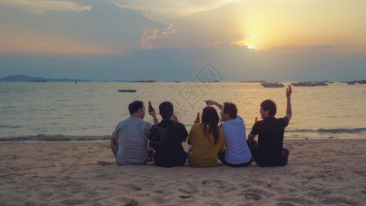 泰国人亚洲朋友串连啤酒瓶子在日落时夏海滩或边庆祝节日图片