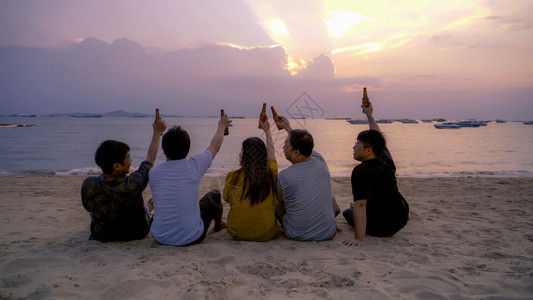 泰国人亚洲朋友串连啤酒瓶子在日落时夏海滩或边庆祝节日图片