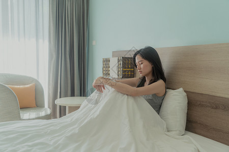 亚裔女在现代卧室里穿着白色毯子思考问题且在床上患忧郁症图片