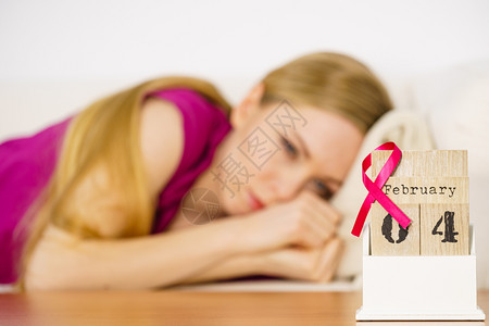预防癌症躺在床上的妇女看着日历今天是4个世界乳癌日与粉红色认识丝带约会保健和医学概念睡觉的妇女日历上世界乳腺癌日背景
