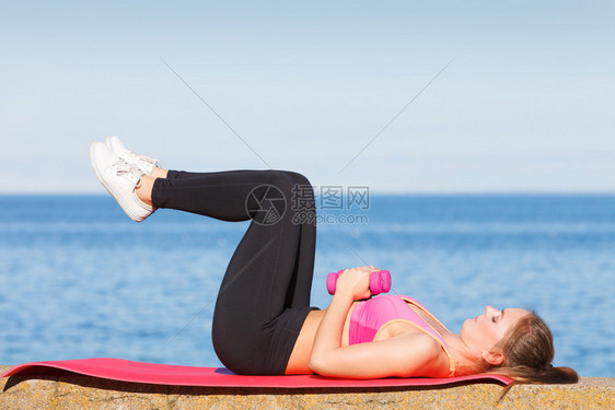 女在户外与哑铃一起运动女在海边运动中穿服的健身女孩在户外与哑铃一起运动图片