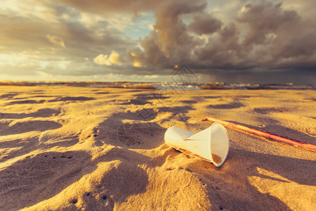 被污染的海滩岸丢弃在沙滩上的塑料可支配杯子背景中的美丽黄金日落地球生态海岸上的塑料可支配杯子地球生态图片