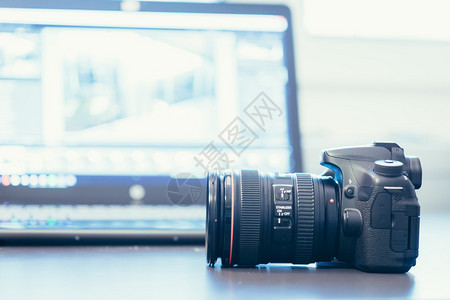 一张桌子上带有远光镜头的专业相机模糊背景的笔记本电脑图片