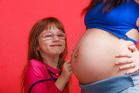 女儿在母亲肚子上使用听诊器背景图片
