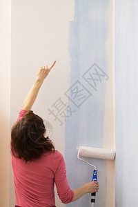 妇女用滚刷在墙上涂油漆家庭翻新概念妇女在墙上涂油漆图片