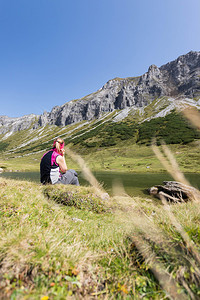 穿运动服的妇女正在徒步时休息坐在地上享受山和湖风景背景图片