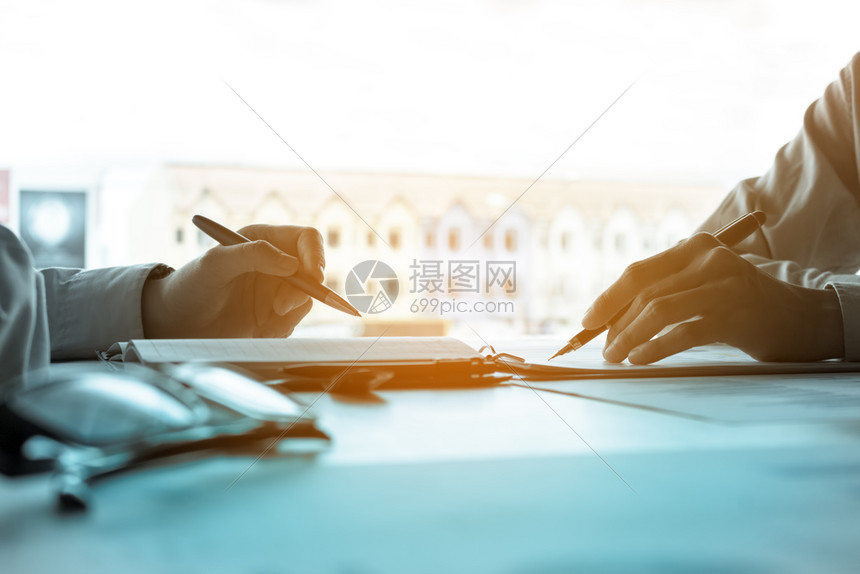 两名持笔的年轻商人指着盈利润在公司房间办室的桌上一起进行分析图片