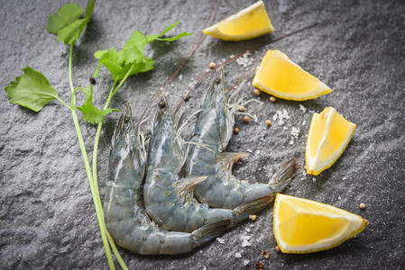 黑盘上生虾新鲜在海产食品餐馆在黑底面配有香料柠檬和菜的新鲜虾图片