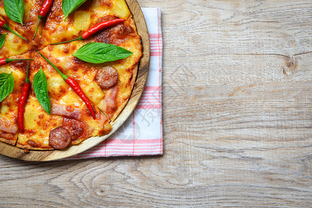 木制餐盘上披萨和辣椒巴西尔叶顶端的风景美味可口的快餐意大利传统比萨奶酪与Mozzarella熏猪肉香肠菠萝火腿加番茄酱复制空间图片