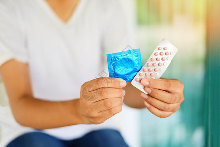 持有避孕药片和套的年轻妇女计划生育避孕手段意味着防止怀孕或传染疾病图片