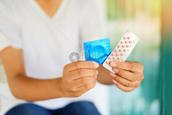 持有避孕药片和套的年轻妇女计划生育避孕手段意味着防止怀孕或传染疾病图片