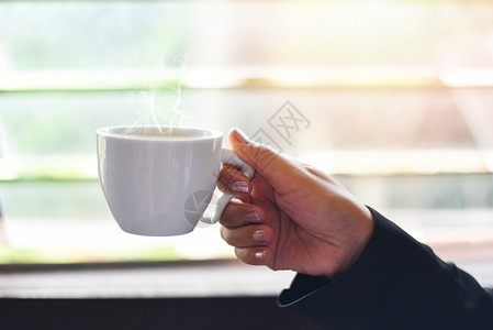白咖啡杯手握着关闭商业妇女拿着咖啡杯窗边的清晨阳光照耀着咖啡杯图片