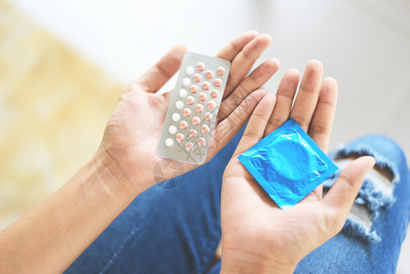持有避孕药片和套的妇女计划生育避孕手段意味着防止怀孕或传染疾病图片