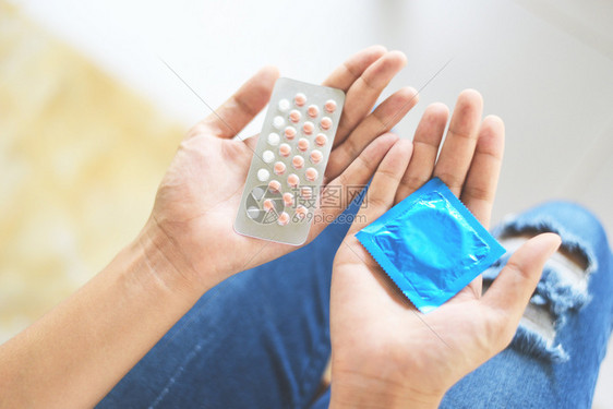 持有避孕药片和套的妇女计划生育避孕手段意味着防止怀孕或传染疾病图片